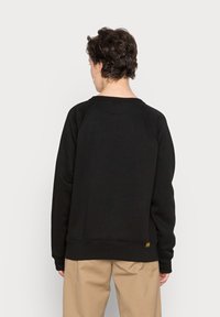 Felpa nera con scollo rotondo, maniche raglan e orlo a costine. Realizzata in tessuto morbido con un dettaglio a toppa vicino al fondo.