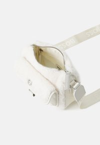 Valge kunstnahast karusnaha efektiga õlakott, millel on nahkdetailid, hõbedane lukutõmme ja logo rihm. Siseosa on helesinine, millel on lukuga tasku.