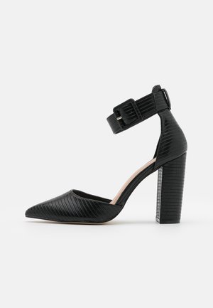 Pampe noire à bout pointu avec une finition texturée, une bride réglable à la cheville et un épais talon bloc. Conçue avec une silhouette élégante.