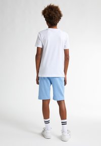 Camiseta blanca de algodón y pantalones cortos azul claro, combinados con zapatillas blancas y calcetines a rayas. Diseño sencillo, corte clásico y textura suave.
