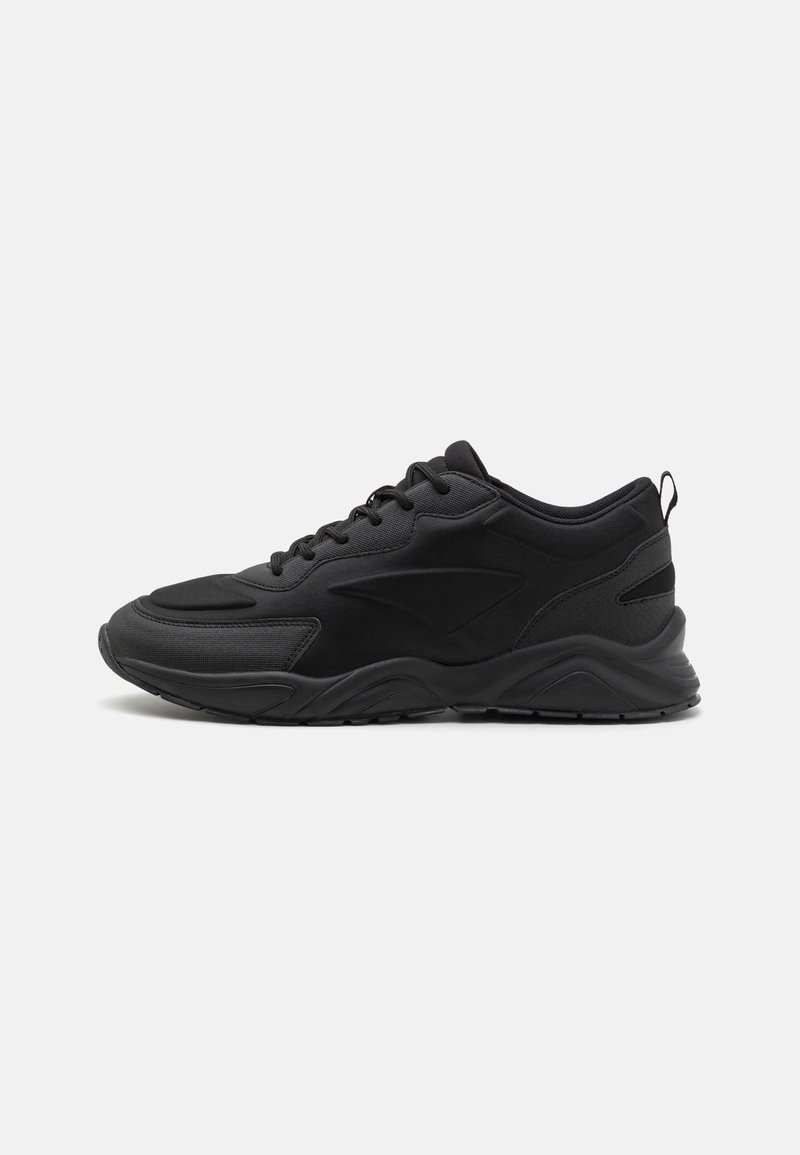 Black athletic shoes with a textured upper, padded collar, and a thick rubber sole. Features a minimalistic design and contrasting accents.