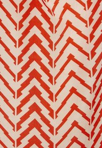 Tessuto con sfondo crema che presenta un motivo a zigzag rosso ripetuto. Il design include angoli affilati e spessori variabili.