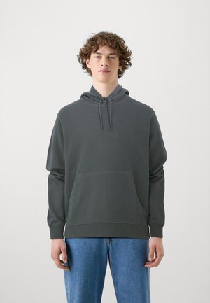 Sweat à capuche gris foncé avec une poche avant, cordon de serrage réglable, et poignets côtelés, associé à un jean bleu clair.