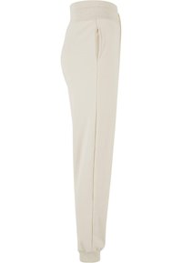 Joggers de algodón beige con cintura acanalada, bolsillos laterales y puños elásticos; textura suave y diseño ajustado.