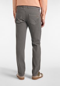 Sive hlače iz bombaža s ravnim krojem, ki vključujejo dvojne zadnje žepe in teksturirane detajle. V kombinaciji z svetlo rjavimi sandali.