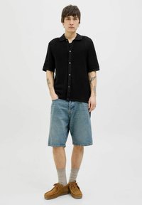 Black short-sleeve knit shirt with a button-up front, paired with light blue denim shorts. Brown shoes and beige socks complete the look.