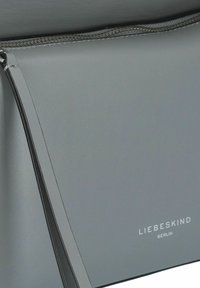 Borsa a tracolla in pelle grigia con una texture liscia, dotata di una tasca frontale con zip e logo "LIEBESKIND BERLIN" in rilievo.