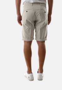 Shorts beige in cotone con risvolti, dotati di tasche posteriori con chiusura a bottone. Abbinati a scarpe da ginnastica bianche. Design semplice e pulito.