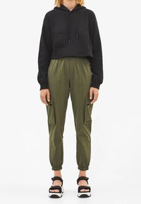 Svart cropped hoodie med en frampocket, kombinerad med olivgröna cargobyxor med sidfickor och elastiska cuffs. Svart och vita sandaler.