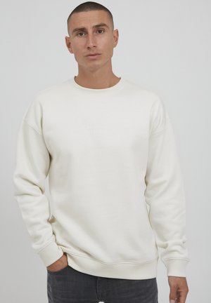 Lichtbeige sweatshirt met een ronde hals, verlaagde schouders en geribde manchetten. Heeft subtiele reliëflettering aan de voorkant. Zachte textuur.