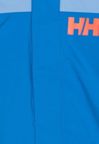 Lyst blå stof med en glat tekstur, prydet med en lys blå vandret stribe og et orange "HH" logo. Lige sømme er synlige.
