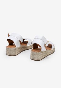 Sandalias de cuña blancas con suelas de yute trenzado, puntera abierta y un diseño de doble tira con un acento de hebilla dorada.