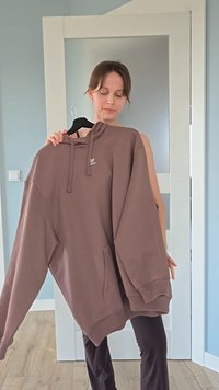 Καφέ oversized φούτερ με κορδόνι, τσέπη καγκουρό και λογότυπο στο στήθος. Λείο υφασμάτινο υλικό, χαλαρή εφαρμογή, κρεμασμένο σε κρεμάστρα.