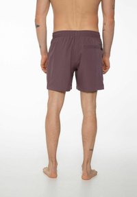 Pantaloncini da nuoto viola corti con elastico in vita, tasca laterale e texture morbida. Presentano tatuaggi visibili sulle gambe.