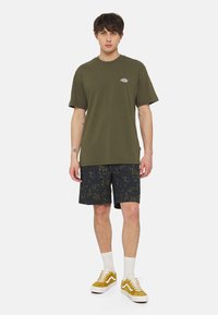 Olivgrön bomullströja med rund hals, kombinerad med marinblå mönstrade shorts och gula sneakers med vita detaljer.