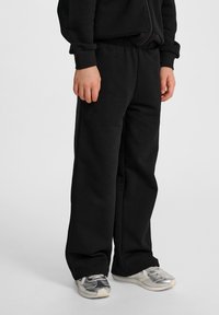Schwarze Sweatpants aus weichem Stoff mit elastischem Bund und geradem Beinverlauf. Getragen mit silbernen Sportsneakern.