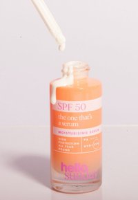 SPF 50 återfuktande serum i en cylindrisk glasflaska med en orange gradient. En pipett dispenserar ett vitt serum. Etiketterna innehåller produktinformation.