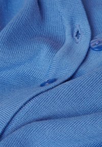 Tissu tricoté bleu avec une texture lisse. Comprend un bouton avec une finition brillante et un petit trou cousu. Des plis délicats créent de la profondeur.