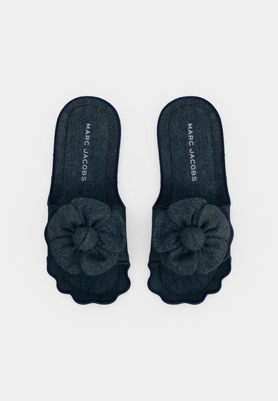 Mørkeblå denim tøfler med stoffblomstdekorasjoner og "MARC JACOBS" trykt inne i hver såle, vist ovenfra på hvit bakgrunn.