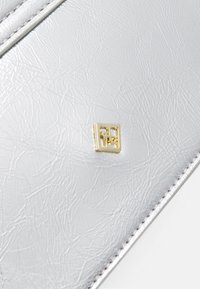Silver textured faux leather with a subtle sheen featuring a gold square logo accent. Edges are stitched with white thread.