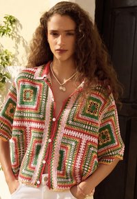 Camisa de crochet abotonada con un patrón geométrico colorido en verde, rojo y rosa, con mangas cortas y un corte relajado.