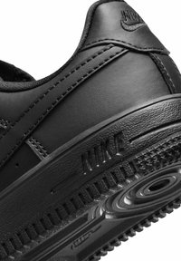 Melna ādas sporta apavi ar teksturētu virsmu, izceltu Nike zīmolu un rakstainu gumijas zoli ar apaļu detaļu. 