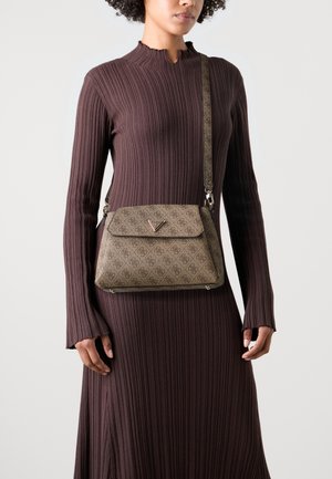 Femme en robe marron côtelée à manches longues portant un sac bandoulière beige avec un rabat et un détail logo métallique.