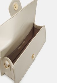 Beige læderhåndtaske med en glat overflade. Har en guldfarvet trykknaplukning og en enkelt indvendig lynlåslomme. Minimalistisk design med afrundede kanter.