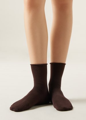 Brune ankelstrømper lavet af et blødt, glat materiale med en ribbet kant, der strækker sig over anklen, vist på bare ben.