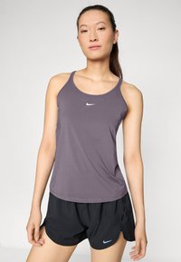 Lilla atletisk tank top med slanke stropper og en rund halsudskæring, parret med sorte shorts med et blåt Nike-logo på kanten.