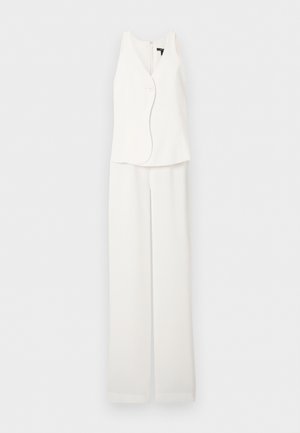 Veste blanche sans manches avec un seul bouton et pantalon large assorti, présentés sur un fond clair uni.