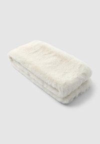 Coperta morbida in finta pelliccia bianca piegata su una superficie grigia chiara e semplice.