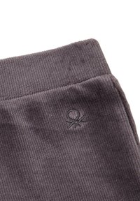 Detailní záběr na tmavě šedou ribovanou látku s elastickým páskem a malým vyšitým logem blízko horního okraje.