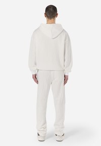 White ribbed hoodie with a hood, loose fit, and dropped shoulders, paired with matching loose-fit pants, showcasing a textured surface.