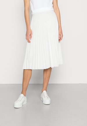 Gonna bianca plissettata con un design svasato, realizzata in tessuto leggero, abbinata a sneaker bianche. Tessuto liscio con una leggera lucentezza.