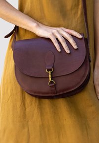 Brown leather crossbody bag with a rounded flap, featuring a gold-tone clasp and curved edges. Smooth texture and a detachable strap.
