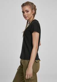 T-shirt en coton noir à manches courtes, avec un col rond et une coupe décontractée, associé à un pantalon cargo olive avec des poches latérales.