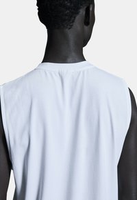 Weißes ärmelloses T-Shirt mit glatter Textur, runder Ausschnitt und genähtem Saum, von hinten vor einem hellen Hintergrund betrachtet.
