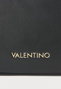 Svart plånbok i läder med guldfärgad "VALENTINO"-logotyp präglad på ytan. Slät textur med en ren, rektangulär design.
