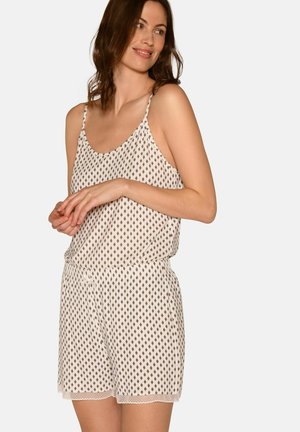 Mujer con camisola sin mangas con estampado y pantalones cortos a juego, sonriendo y mirando hacia un lado sobre un fondo liso.