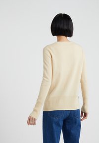 Pull beige clair en matériau doux, doté de manches longues et d'un ourlet côtelé, associé à un jean en denim bleu.