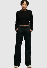 Maglione cropped nero a maglia con scollo rotondo, abbinato a pantaloni neri a gamba larga. Entrambi sono realizzati in un tessuto morbido con una finitura testurizzata.