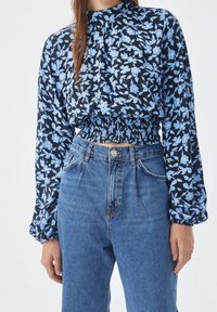 Top court à imprimé floral bleu marine avec des fleurs bleu clair, doté d'une taille froncée et de manches longues bouffantes ; associé à un jean en denim taille haute.