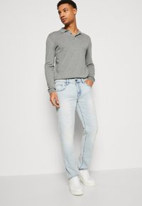 Gray long-sleeve polo with a collar, paired with light blue denim jeans. White sneakers complete the outfit. Simple and casual design.