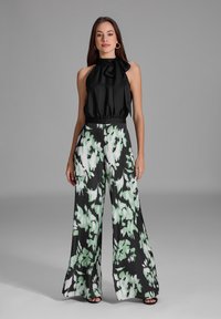 Haut halter noir avec un détail de cou noué, assorti �à un pantalon large taille haute présentant un motif floral vert et noir.