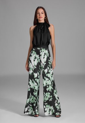 Haut halter noir avec un détail de cou noué, assorti à un pantalon large taille haute présentant un motif floral vert et noir.