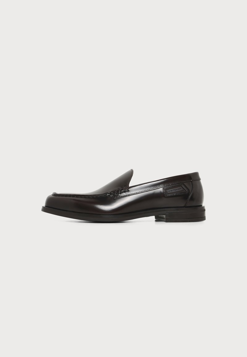 Μαύρο ανδρικό δερμάτινο παπούτσι τύπου slip-on με χαμηλό τακούνι και ραφές εμπρός και στα πλάγια σε λευκό φόντο.