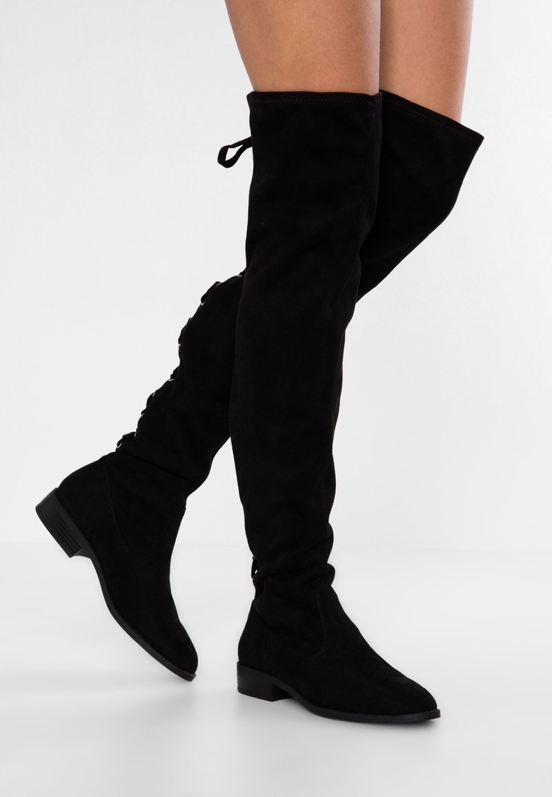 Bottes noires au-dessus du genou en daim, avec un bout effilé et un petit talon carré, dotées de lacets à l'arrière pour un ajustement réglable.