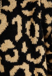 Stickad tyg med svart bas och stora bruna leopardprickar. Mjuk textur med synlig sömnad och fibrer.