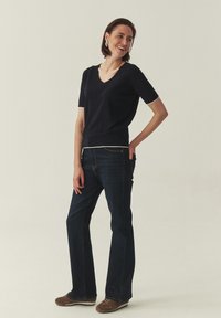 Suéter azul marino de manga corta con cuello en V y ribetes blancos, combinado con jeans azul oscuro acampanados y zapatos marrones. Textura suave y diseño ajustado.